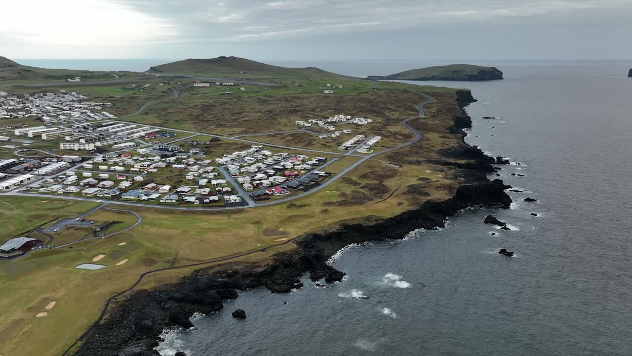 Aerial view of a coastal settlement on Heimaey Island, Iceland, highlighting volcanic terrain, basalt cliffs, and the North Atlantic.