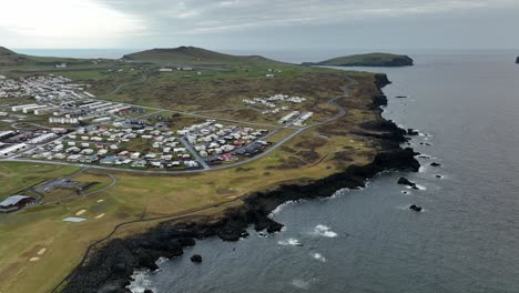 aerial view of a coastal settlement on heimaey island, iceland, highlighting volcanic terrain, basalt cliffs, and the north atlantic.
