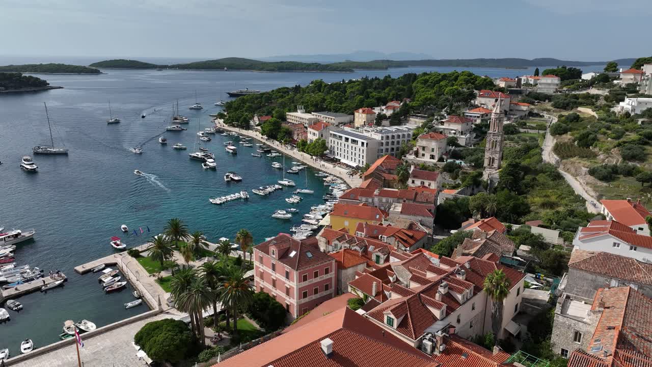Drone flight over Hvar coastline with historic buildings and St. Mark's Church bell tower.