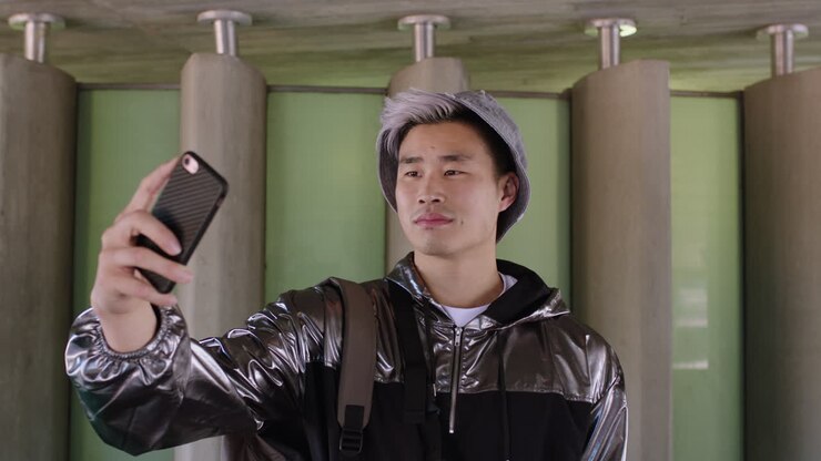 Ritratto di giovane studente asiatico alla moda che si scatta un selfie buffo e divertente.