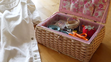 a sewing kit with pin cushion, tape measures, needle and thread on a table for a seamstress to repair a white dress shirt