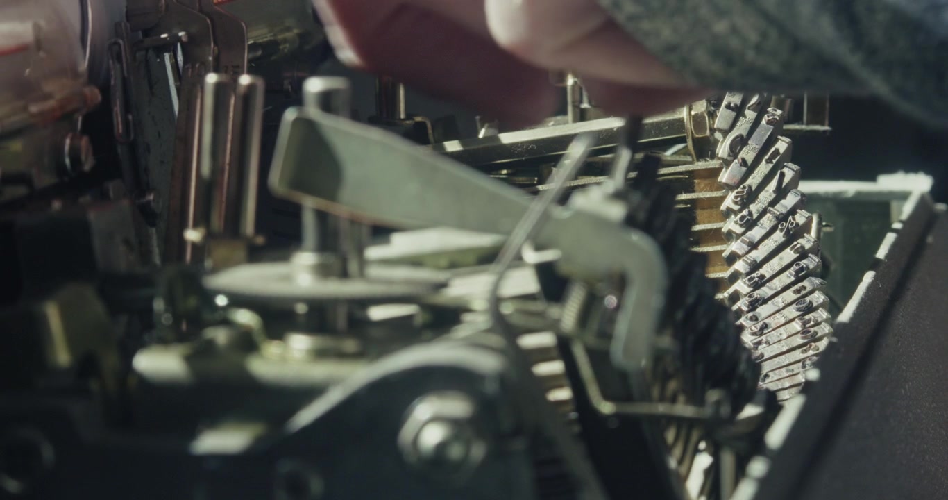 Close-up of a mechanical typewriter experiencing a typebar jam before the operator gently frees the mechanism, illustrating maintenance and analogue office technology.