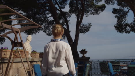 a stylish girl walks through patio to railing overlooking the italian sea