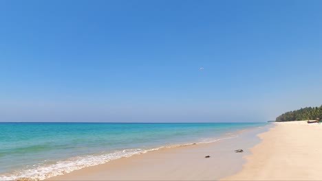 wide-angle view of blue sky white sand beach in clear air sunny day. a white seagull fly through the clear blue sky. tourism in tropical paradise southern sea in thailand. water waves ripple on shore