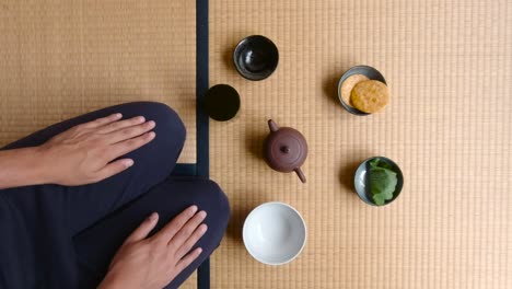 hombre sentado en una alfombra de tatami comiendo galletas y bocadillos japoneses tradicionales durante la hora del té - tiro medio