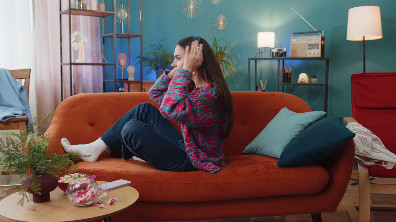 Happy woman in wireless headphones relaxing resting lying on couch at home listening favorite music