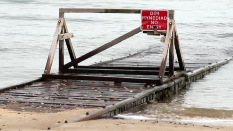 tide in on flooded seaside wooden plank walkway jetty with welsh caution warning sign