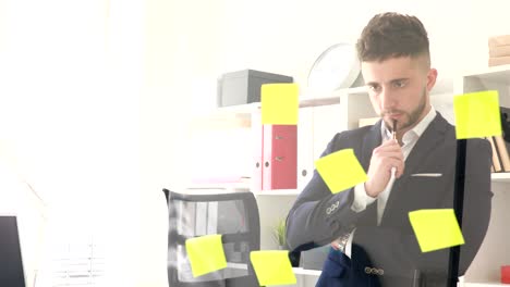 businessman with pen in hand thinking near glass wall