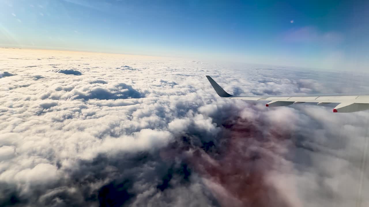 En passagerflyvinge glider over et tæt lag af hvide skyer under klart sollys