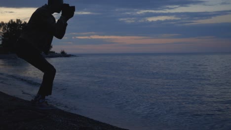 man seeks to capture beautiful sunset with camera by the beach - medium shot