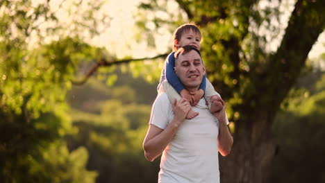 A-child-sitting-on-the-neck-of-his-father-while-walking-in-summer-field-at-sunset.