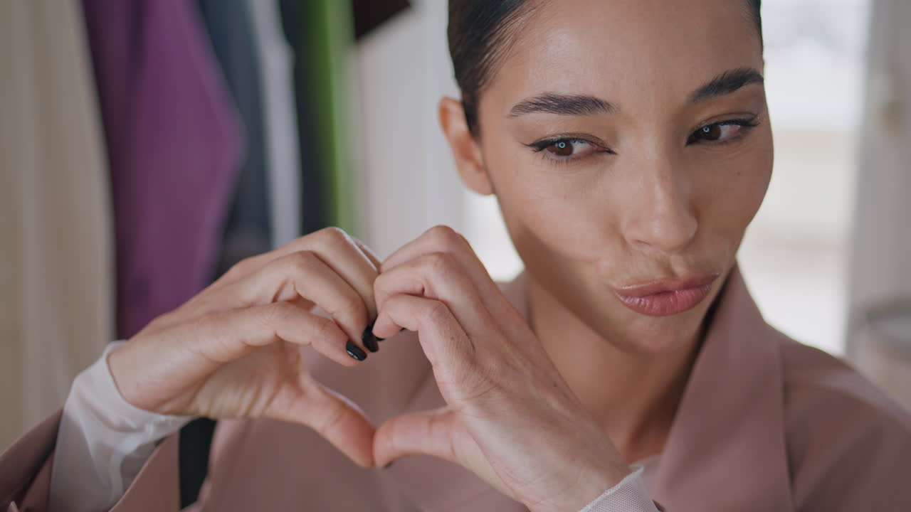 집에서 심장 모양의 몸짓을 하는 여자. 웃는 블로거가 온라인에서 이야기합니다.