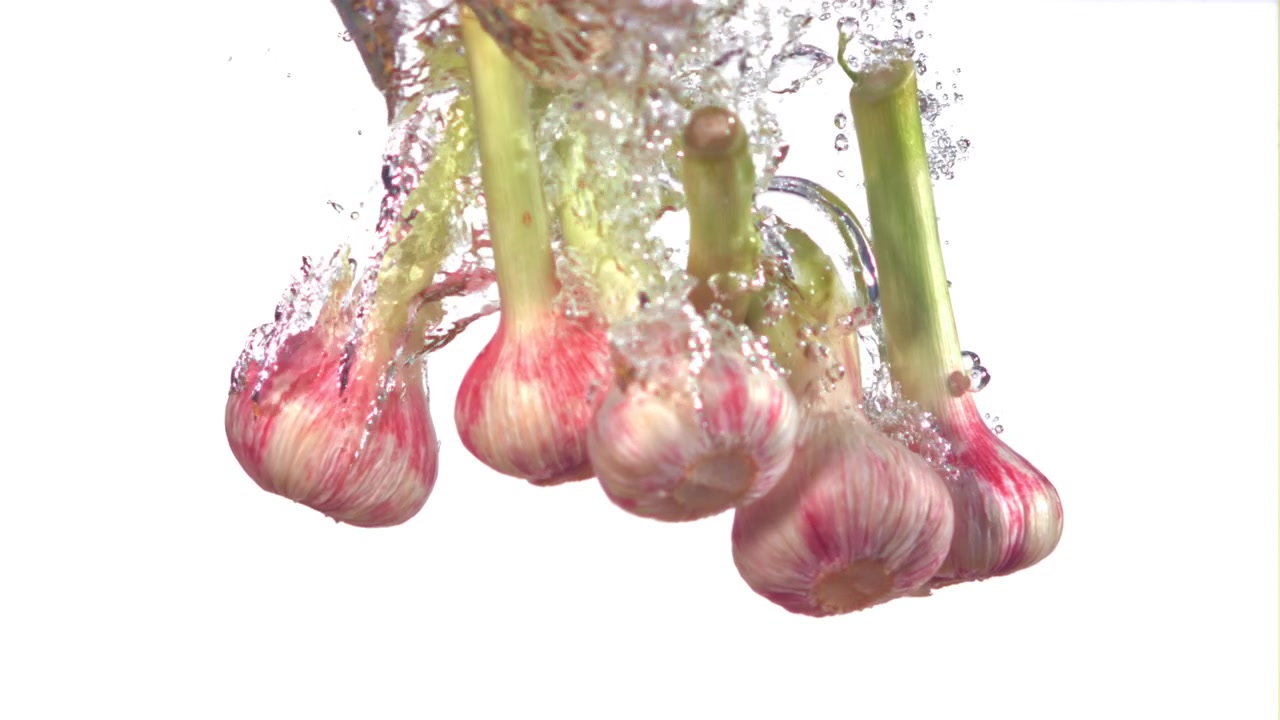 Bulbi d'aglio freschi con steli verdi che cadono in acqua