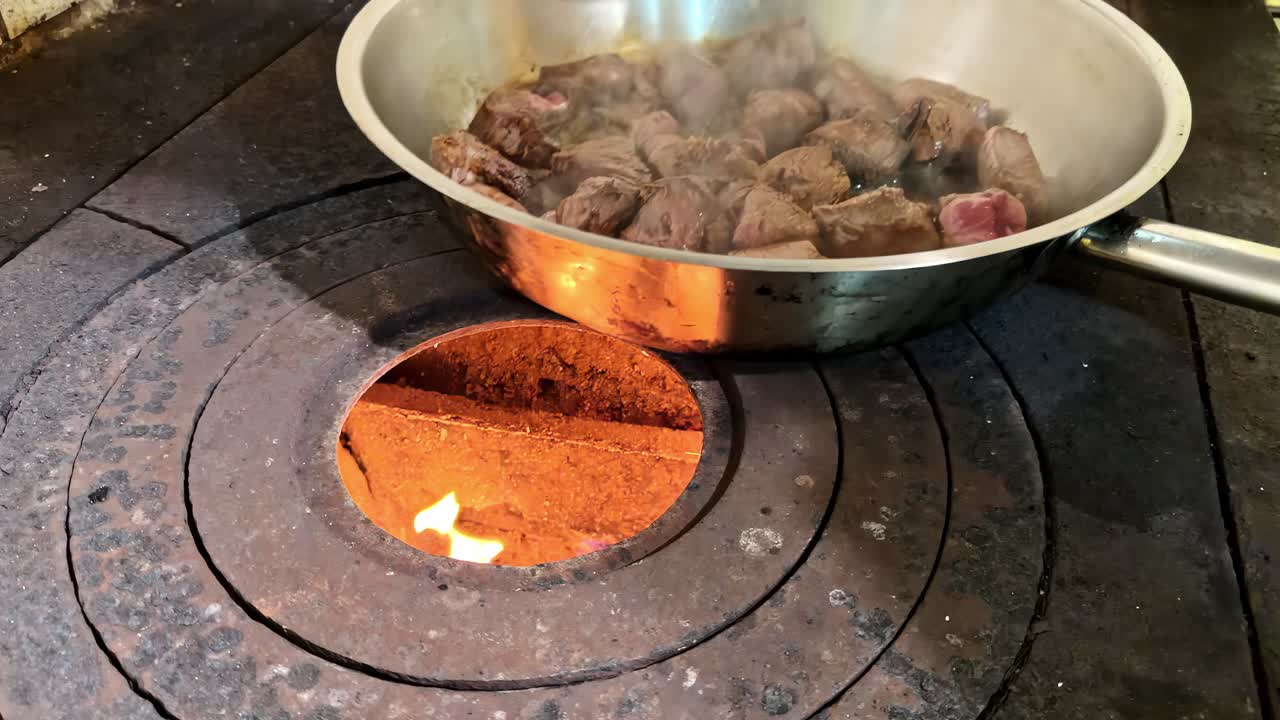 Chunks of wild game meat searing in metal pan on stovetop during rustic cooking process