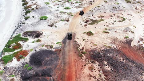 Following-two-buggies-driving-through-empty-desert-volcanic-land-on-off-road-track-under-mid-day-sun