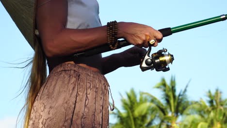 Close-up-shot-of-pretty-woman-fishing-with-rod-at-beach-of-ocean-with-tropical-palm-trees-in-backdrop