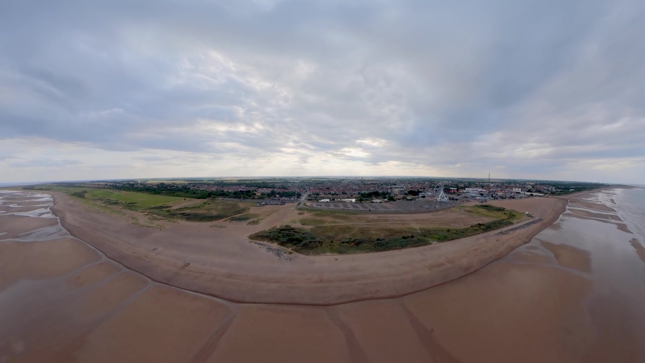 英国林肯郡沙滩和沙丘的鸟瞰航拍图，海浪拍打着海岸。日落时分，一人带着两只狗在沙滩上散步。