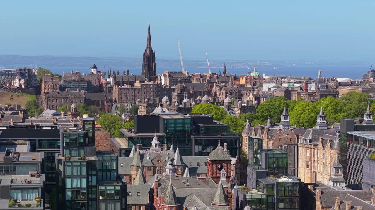 Drone footage over Edinburgh highlighting The Hub at the city center, showcasing its gothic spire and the surrounding urban landscape on a clear day