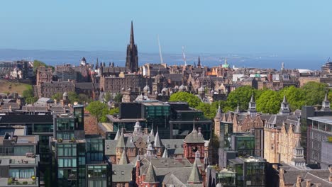 drone footage over edinburgh highlighting the hub at the city center, showcasing its gothic spire and the surrounding urban landscape on a clear day