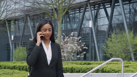 businesswoman commuting to work talking on mobile phone outside modern office building