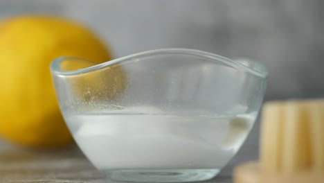 a close-up of a glass bowl containing a white substance and water, with a blurred lemon in the background