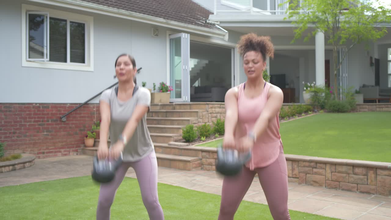 Những người phụ nữ đa dạng sau khi nhìn lướt qua, nhặt tạ chuông ở sân sau, kiểm tra độ bám và vung tạ để tập luyện.