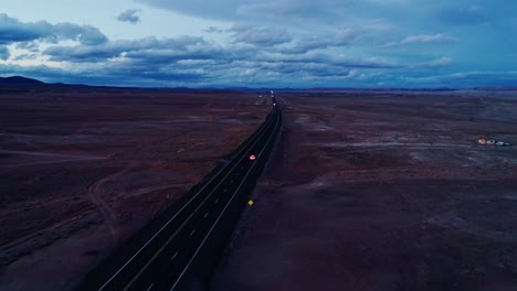 remote highway vanishing into desert dusk with red car lights in distance, drone