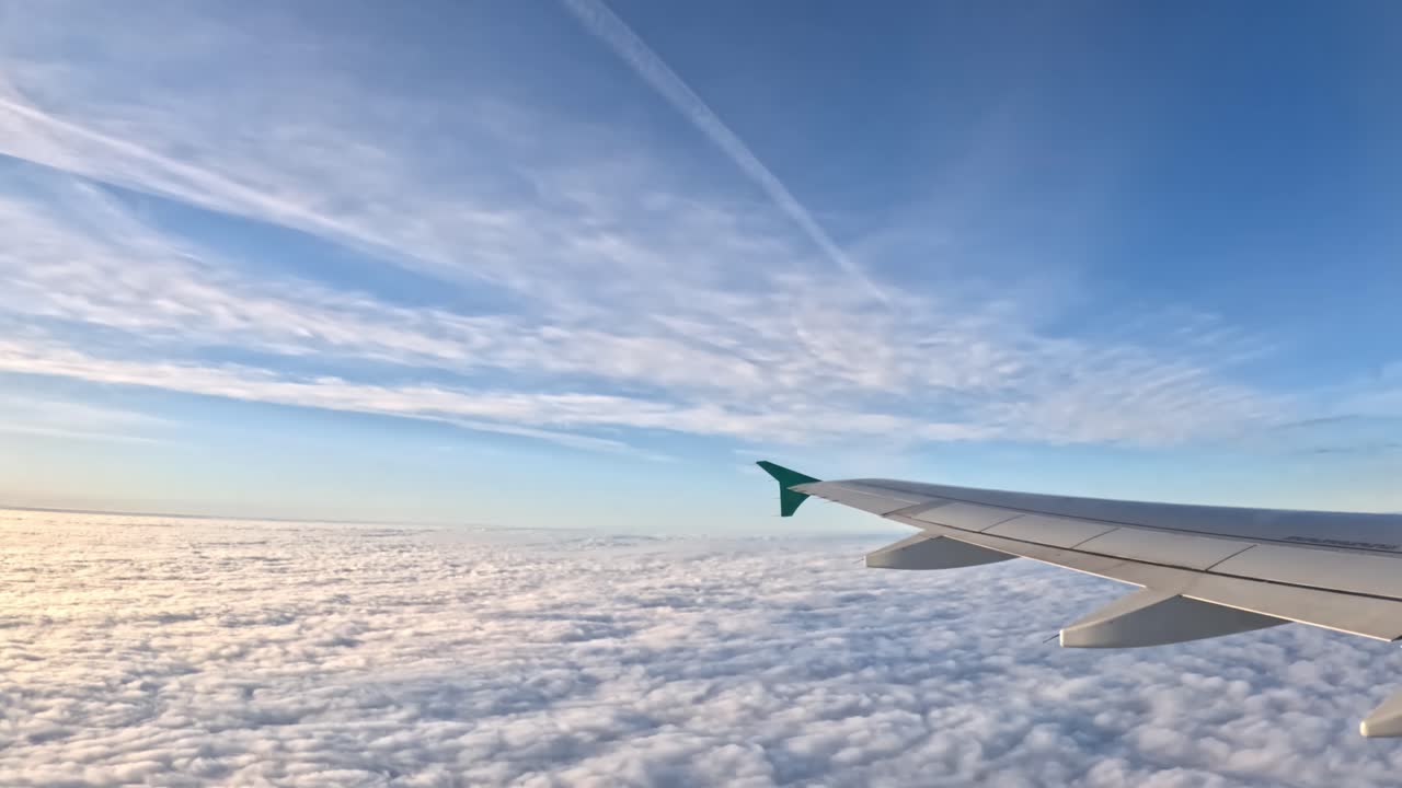 Airplane wing soaring above dense cloud layer during international flight, contrails stretching across bright sky, wide angle perspective capturing aerial journey between Latvia and Germany
