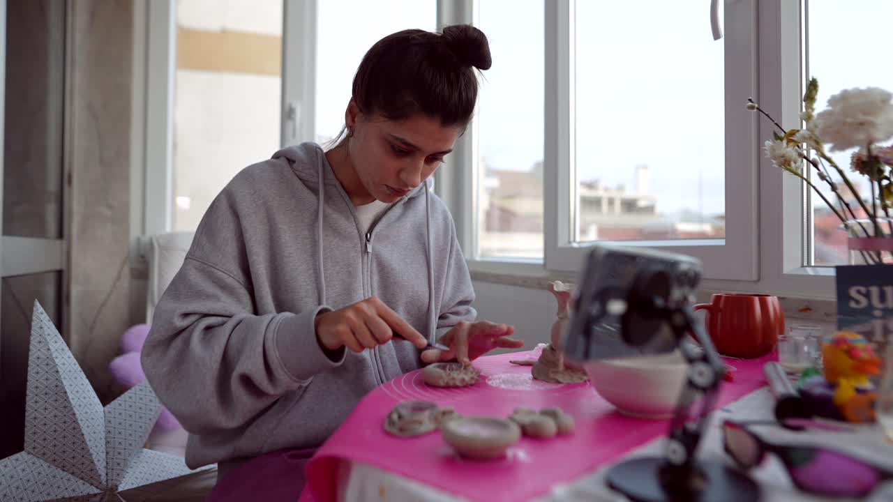 Giovane donna che scolpisce statuette di argilla nel suo studio casalingo.