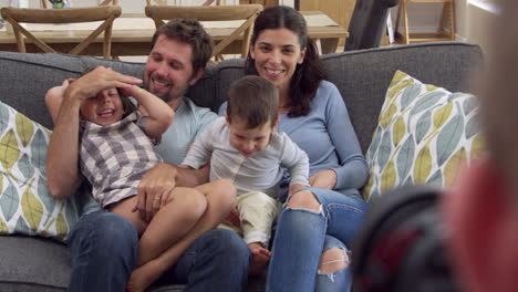 smiling family sit on sofa at home having photograph taken