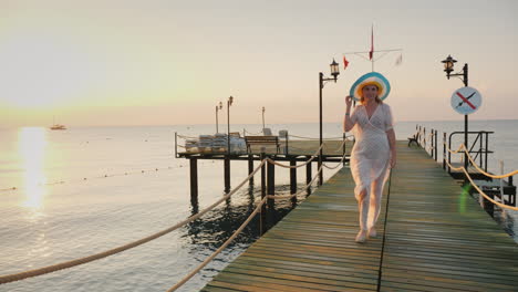 a woman in a pair and hat walks on the pier in the early morning breathes in the fresh air steadicam