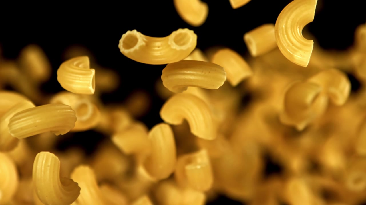Maccheroni crudi che cadono al rallentatore su sfondo nero