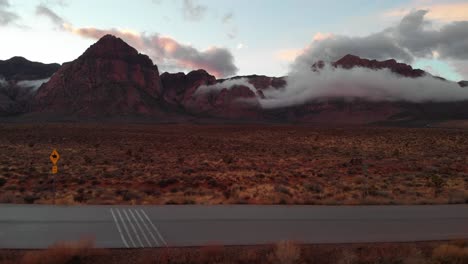 aerial drone shot of an empty road with mountains in the background at sunset