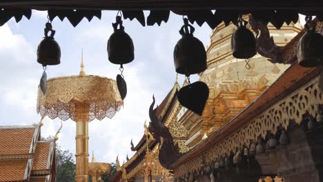Row-of-small-temple-bells-hanging-from-the-eaves-with-background-of-gold-plated-chedi-and-buildings-at-Wat-Phra-That-Doi-Suthep,-one-of-the-most-famous-Buddhist-temple-in-Chiang-Mai,-Thailand