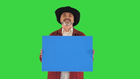 smiling senior man in a hat holding blank placard on a green screen, chroma key