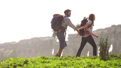 young lovely couple backpackers tourists walking holding hands toward roman aqueduct arches in parco degli acquedotti park ruins in rome on romantic misty sunrise with guitar and sleeping bag slow motion