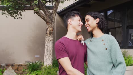 Portrait-of-happy-diverse-male-moving-house,-holding-keys,-embracing-and-smiling