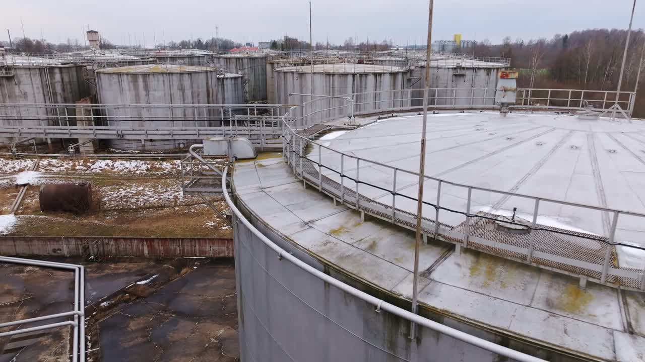 Overcast drone shot flying forward above snowy fuel tanks in rural Latvia