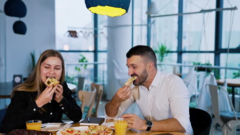 colleagues having pizza in the café. man and woman sit at table enjoying food greatly. people talk and laugh eating.
