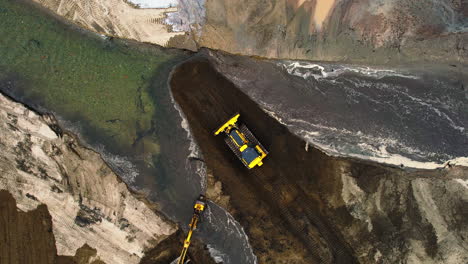 ascending top down aerial view of bulldozer and excavator moving soil in front of water channel at pond site