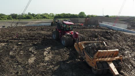 Aéreo,-Tractor-Tirando-De-Un-Carro-De-Remolque-Hasta-Una-Pequeña-Colina-En-Un-Sitio-De-Construcción-Rural