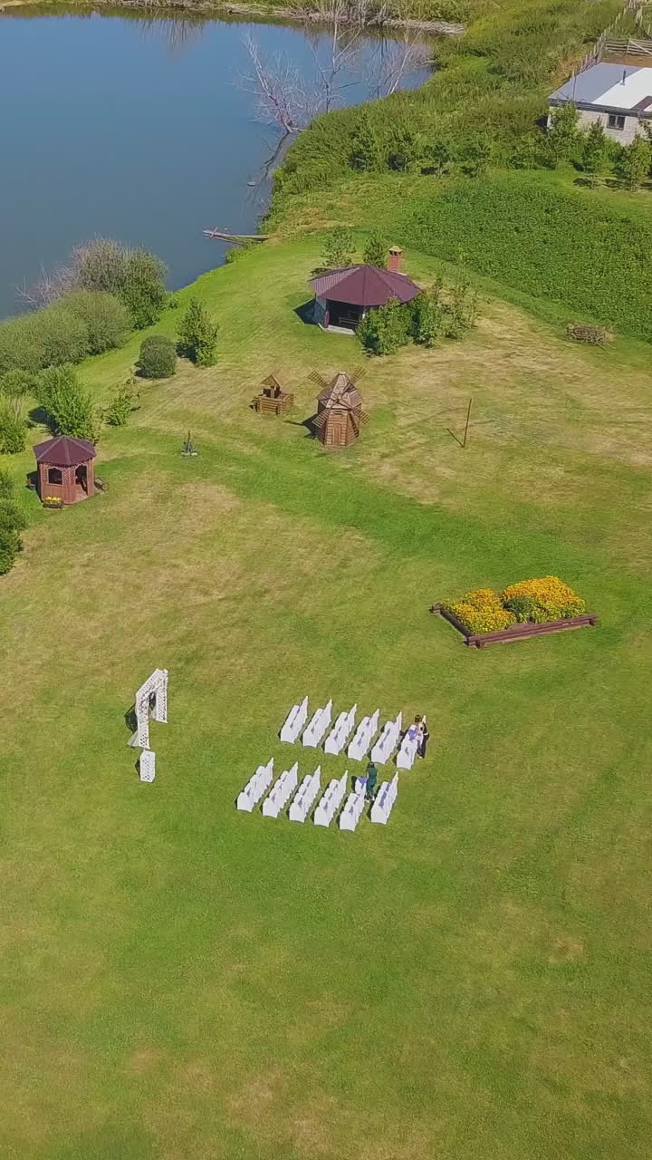 lush green field with different wedding decorations at calm lake on warm autumn day aerial view