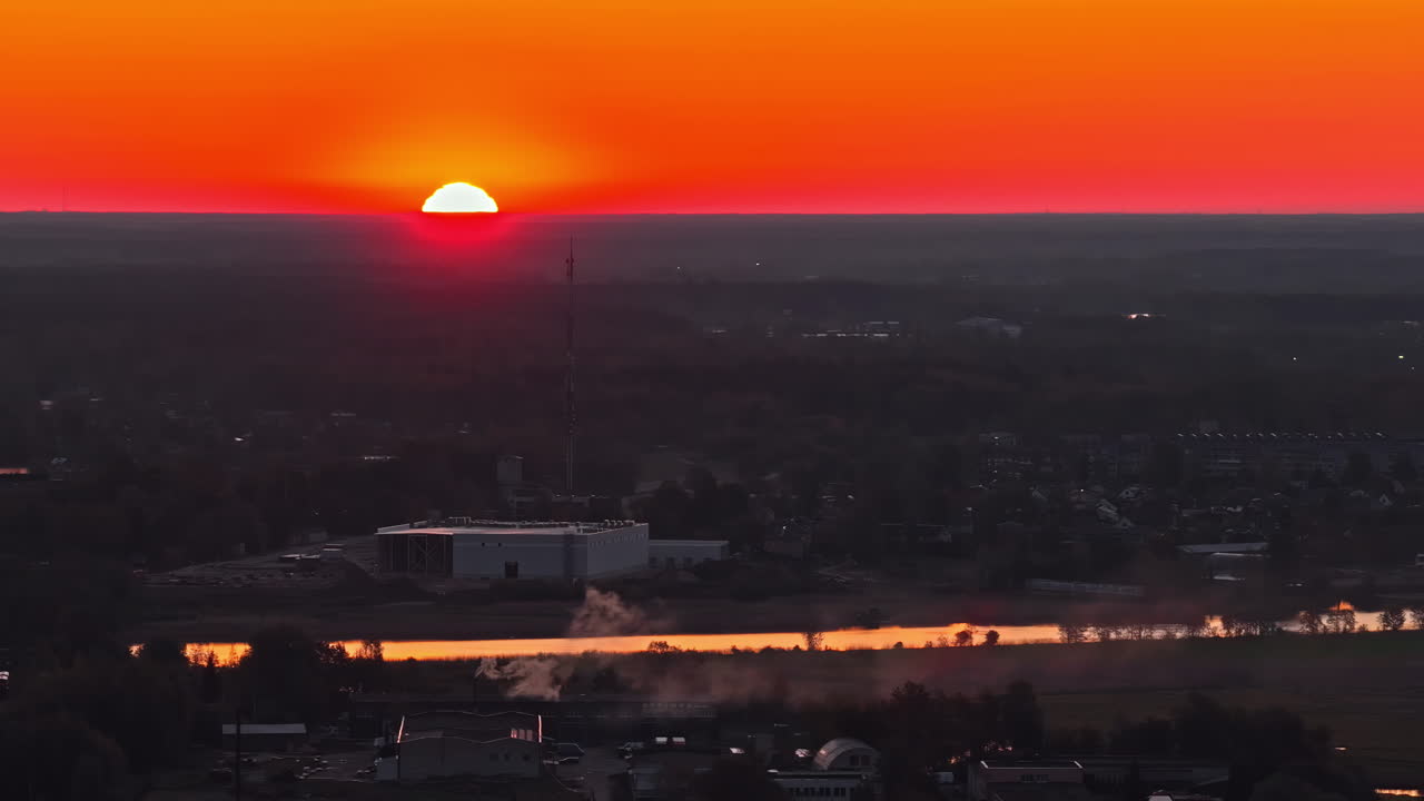 Sunset behind industrial building with smokestack overlooking rural landscape and river