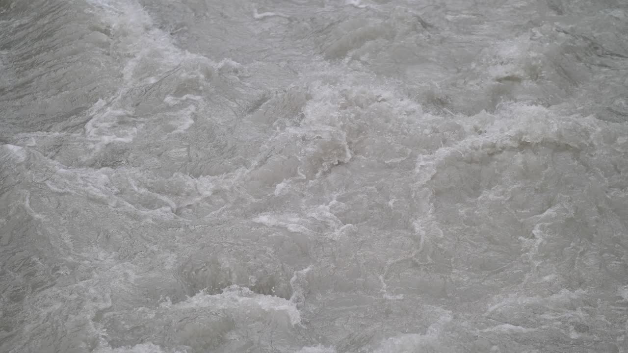 Fast streaming gray melted water in a small river and sloshing on the rocks and stones in Lauterbrunnen Switserland. Close-up shot