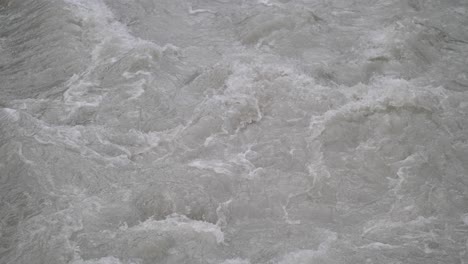 fast streaming gray melted water in a small river and sloshing on the rocks and stones in lauterbrunnen switserland. close-up shot