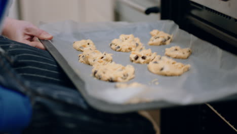 little boy helping mother bake in kitchen putting homemade cookies in oven wearing oven mitts enjoying fresh delicious treats