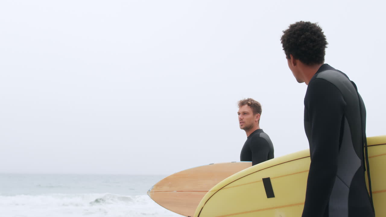 vista lateral de dos surfistas masculinos de pie con una tabla de surf en la playa 4k