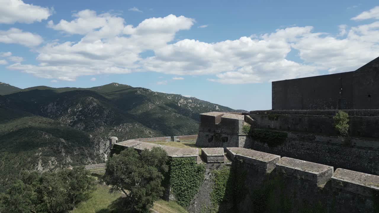 Basking in sunlight, fort de bellegarde stands majestically as puffy white clouds drift across a vibrant blue sky, showcasing the beauty of the french countryside on a serene summer day, orbital drone