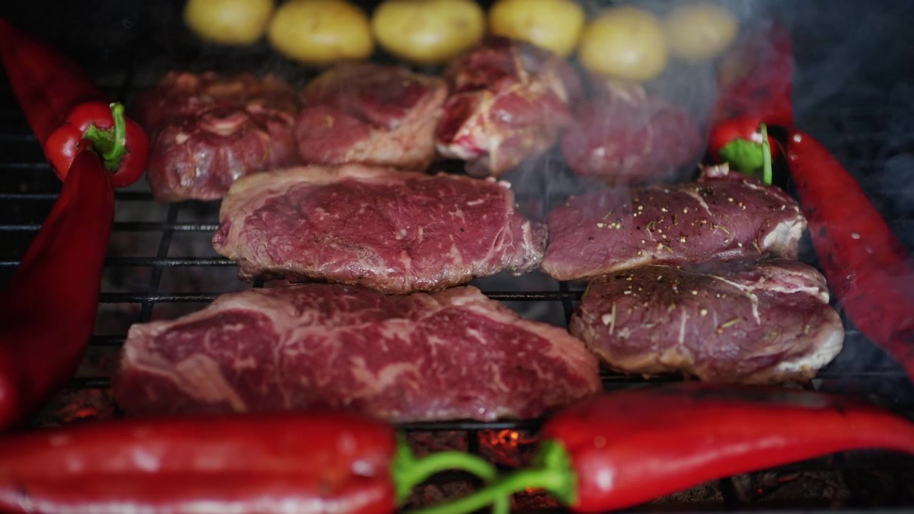 Carne a la parrilla con marcas de sellado visibles, volteándose mientras se cocina sobre brasas calientes junto a verduras