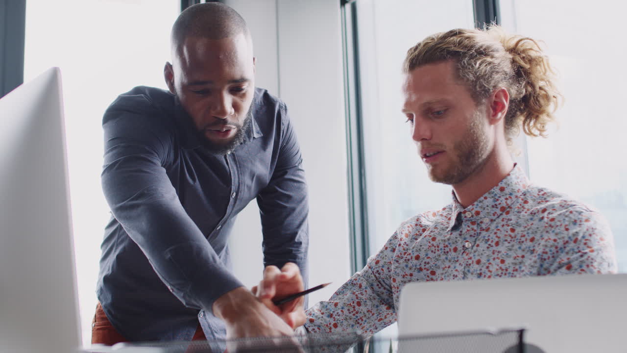 Two male colleagues in discussion at a computer monitor in a creative office, low angle, close up